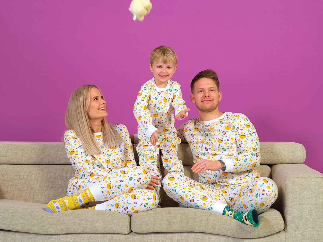 En mand, en dame og et barn sidder sammen i en sofa og er iført hvide påskepyjamas.